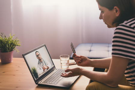 Eine Frau sitzt auf einem Sofa und unterhält sich über ihren Laptop online mit einem Arzt. Konzept der Telemedizin. 